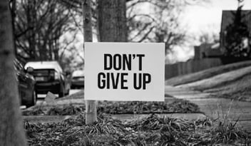 An outdoor sign displaying 'Don't give up' in full caps